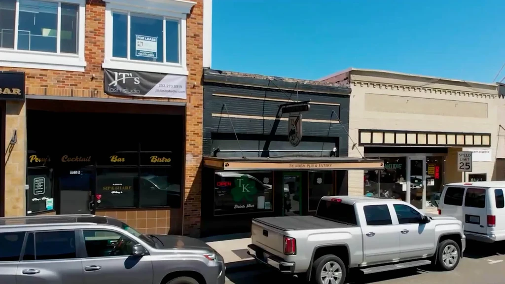 Commercial street with bar, pub, antique store, and two parked vehicles.