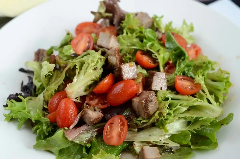 Fresh salad with mixed greens, halved red tomatoes, and cooked protein.
