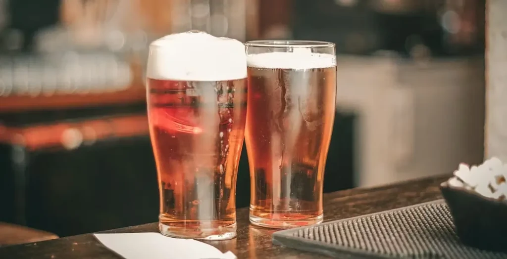 Two tall glasses of amber beer on a dark bar with popcorn.