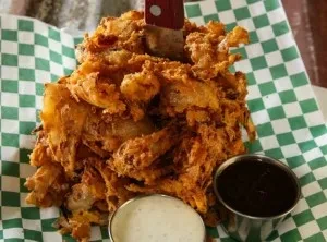 Large blooming onion appetizer with a knife and two dipping sauces.