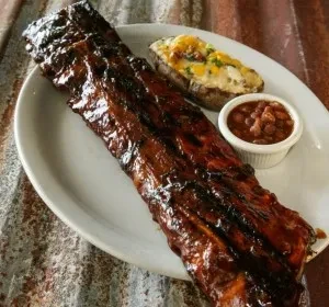 Glazed barbecue ribs, cheese potato, and baked beans on a plate.