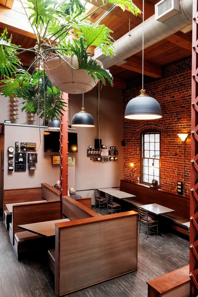 Modern industrial restaurant with brick, wood, green plant, and two people.