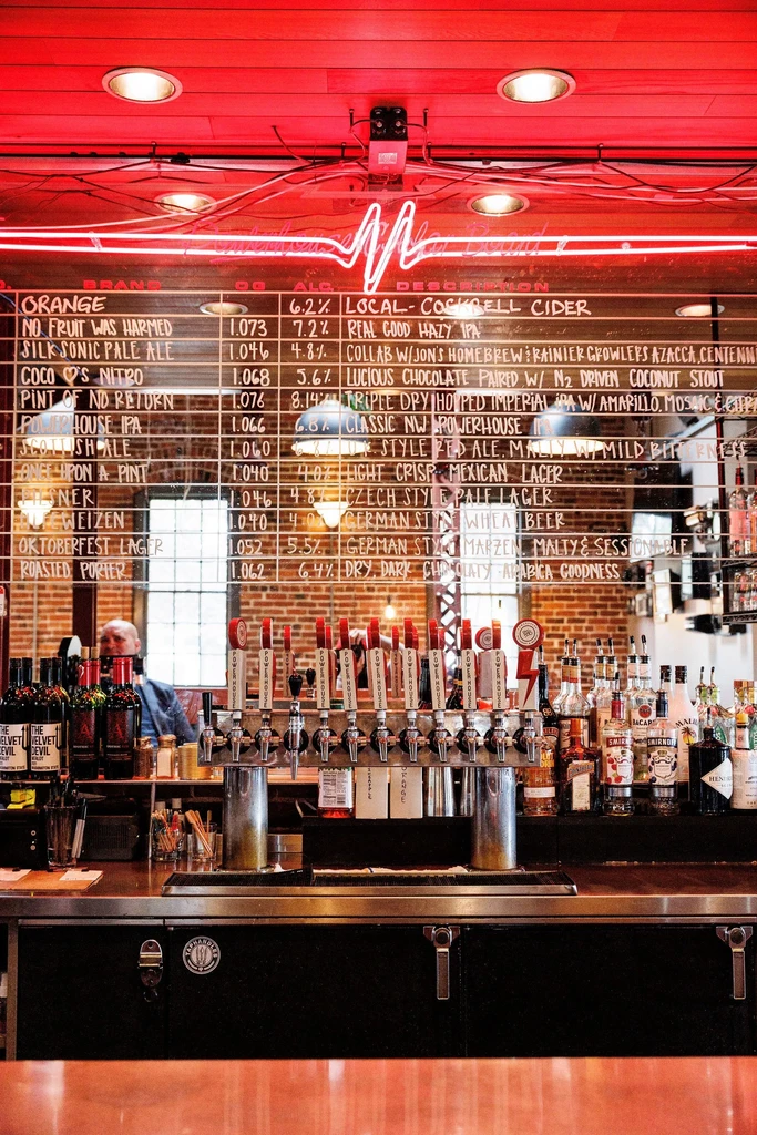 Modern bar with taps, liquor, and red neon menu.