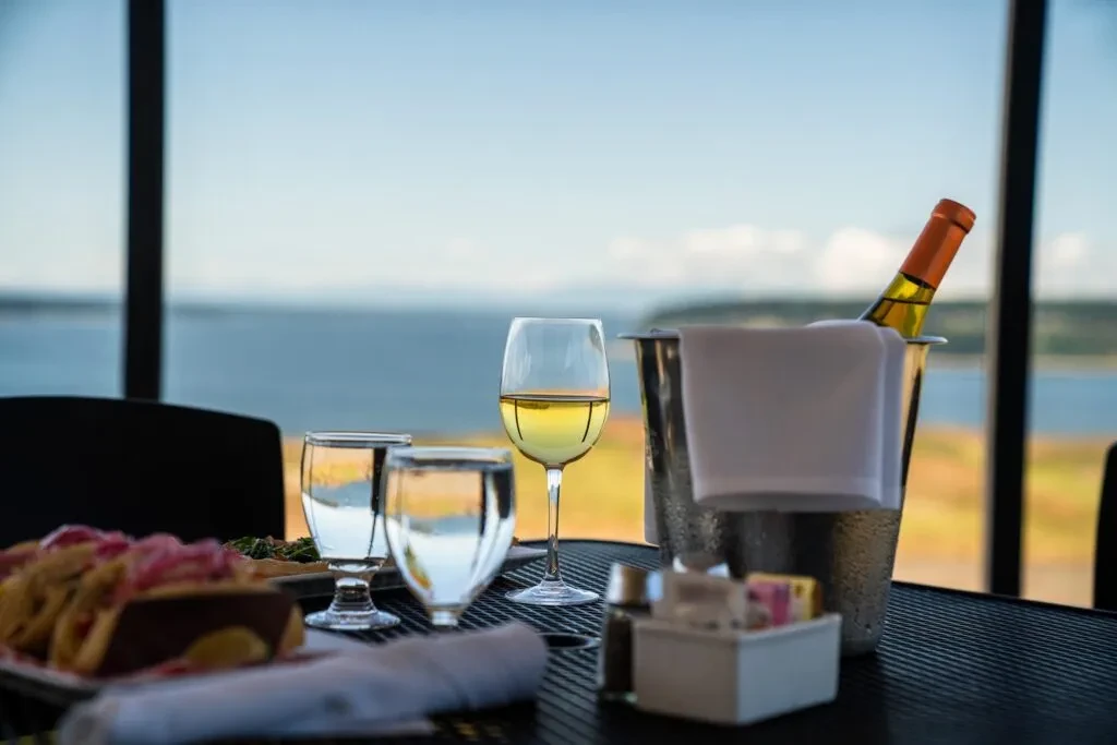 Dining table with wine, water, food, and ice bucket overlooking water.