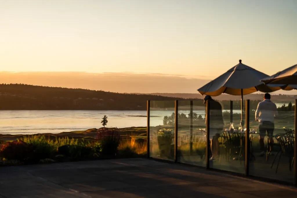 Restaurant patio overlooks a lake, forested land, and sunset sky.