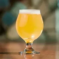 Hazy golden beer in tulip glass with white head on wood.