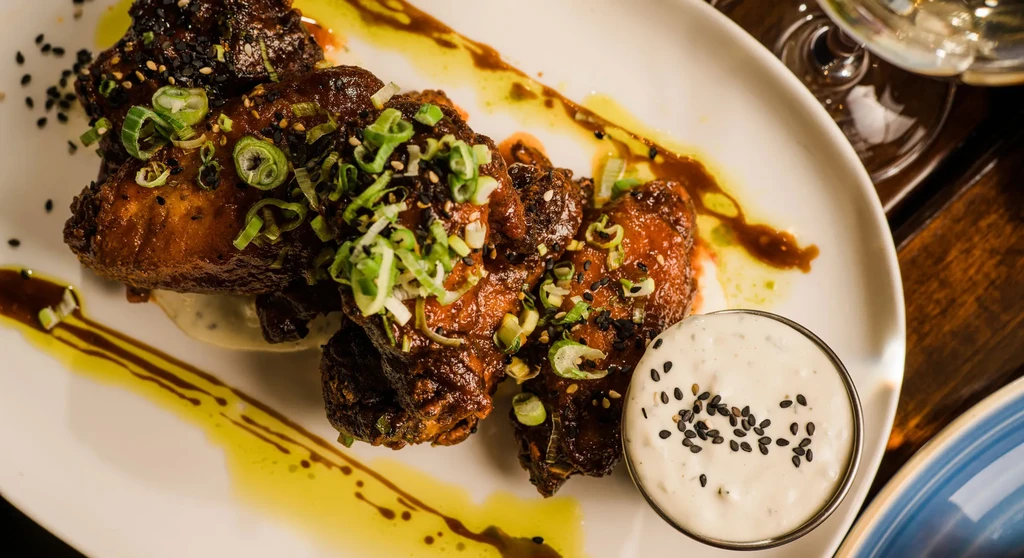 Glossy chicken wings with green onions, sesame seeds, and dipping sauce.