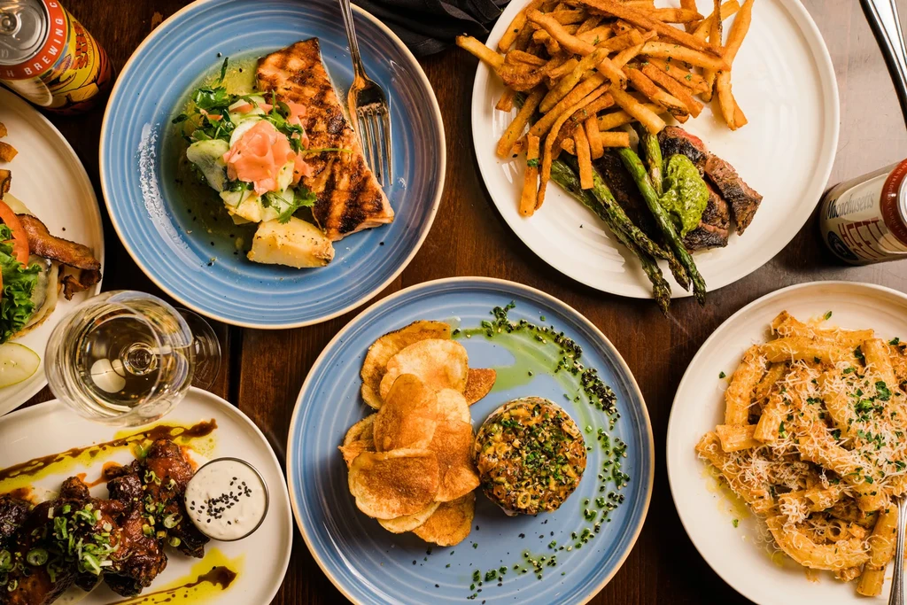 Overhead view of a wooden table with diverse restaurant dishes and drinks.