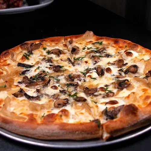 Sliced white pizza with mushrooms and green herbs on a metal tray.