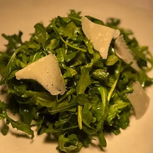 Close-up of fresh arugula salad topped with Parmesan cheese shavings.