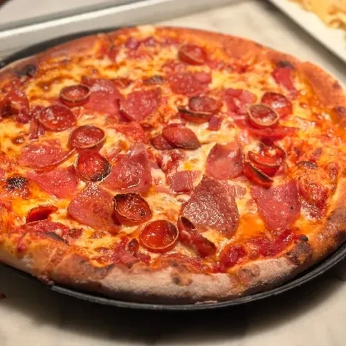 Freshly baked pepperoni pizza with melted cheese and golden crust on a dark pan.