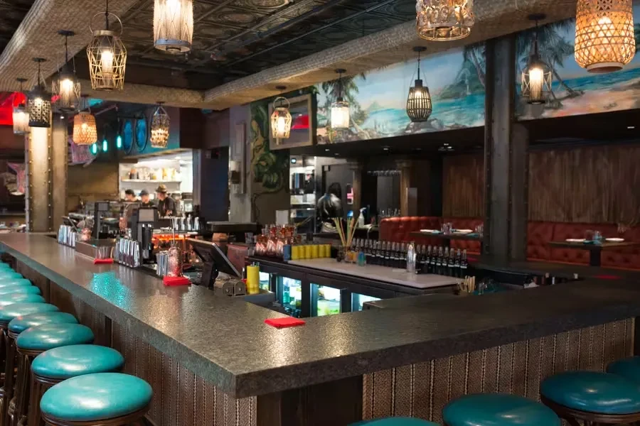 Warm tropical-themed bar interior with teal stools and beach mural.