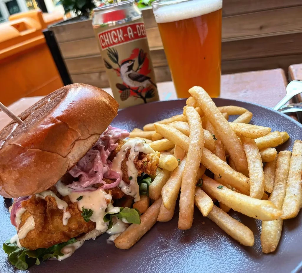 Fried chicken sandwich, seasoned fries, and a beer on a patio table.