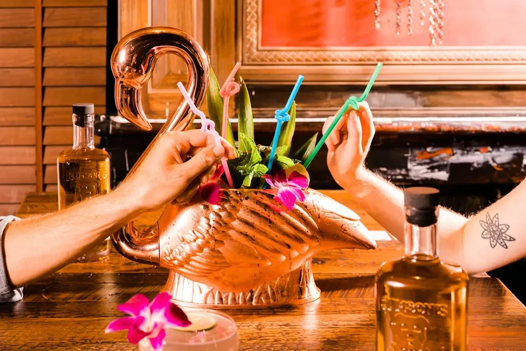 Copper flamingo punch bowl with cocktail, mint, orchids, and two hands with straws.