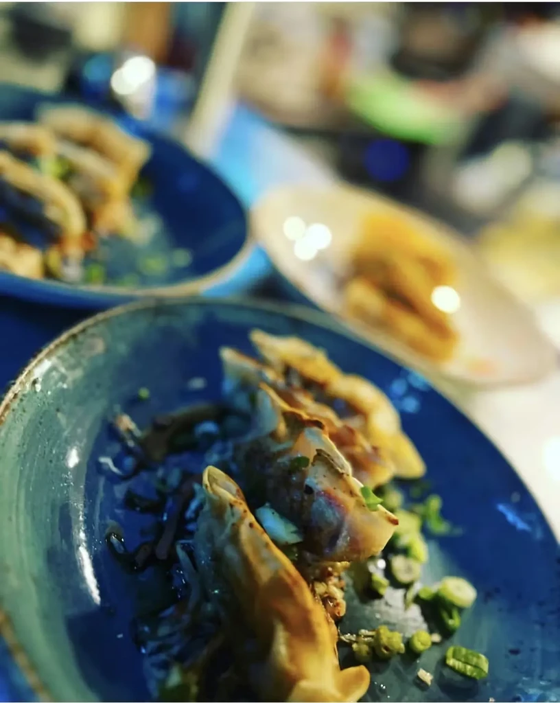 Golden-brown fried dumplings with green onions on a dark blue plate.