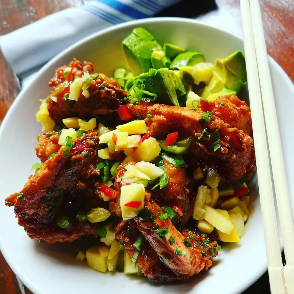 White bowl of sauced fried food, colorful salsa, avocado, and chopsticks.