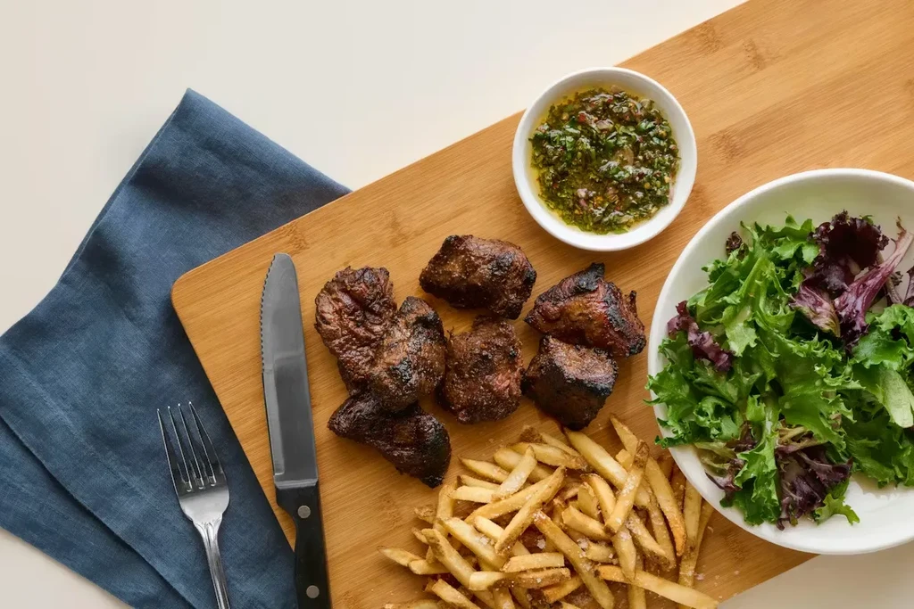 Top-down view of grilled meat, fries, salad, and green sauce.