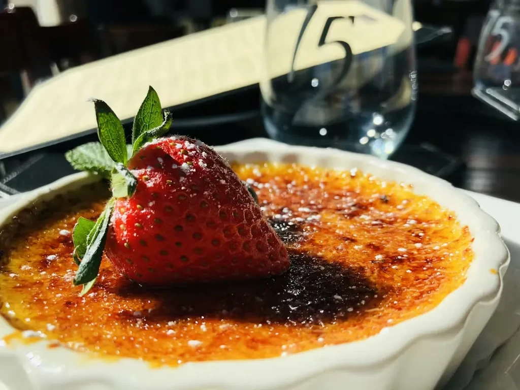 Crème brûlée with caramelized sugar, strawberry, mint, and powdered sugar.