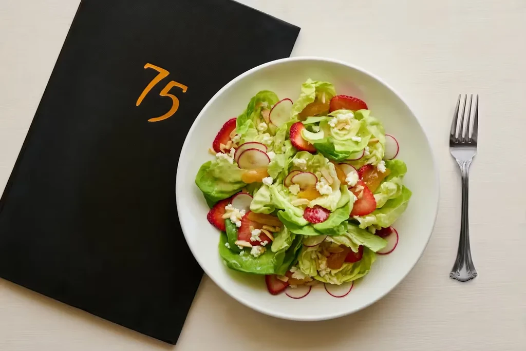 Overhead: Salad with strawberries, radishes, black menu, and fork.
