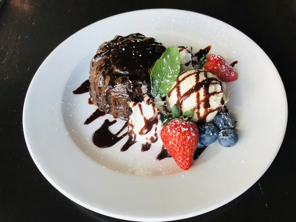 Dark chocolate dessert with vanilla ice cream, berries, whipped cream, mint.