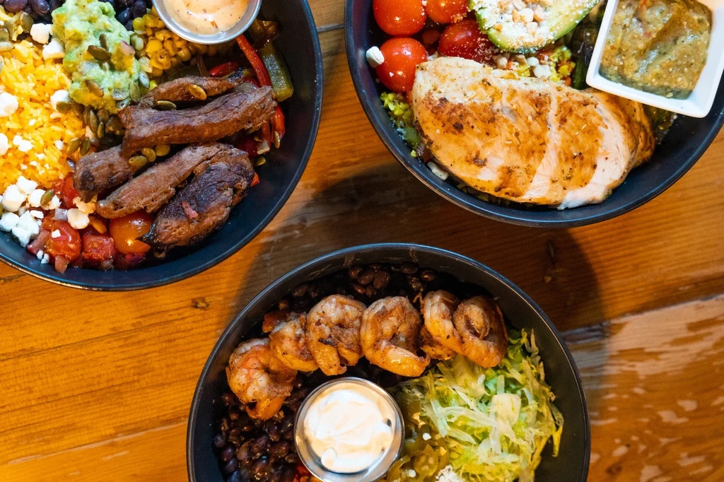 Colorful overhead view of three bowls with grilled steak, chicken, shrimp.
