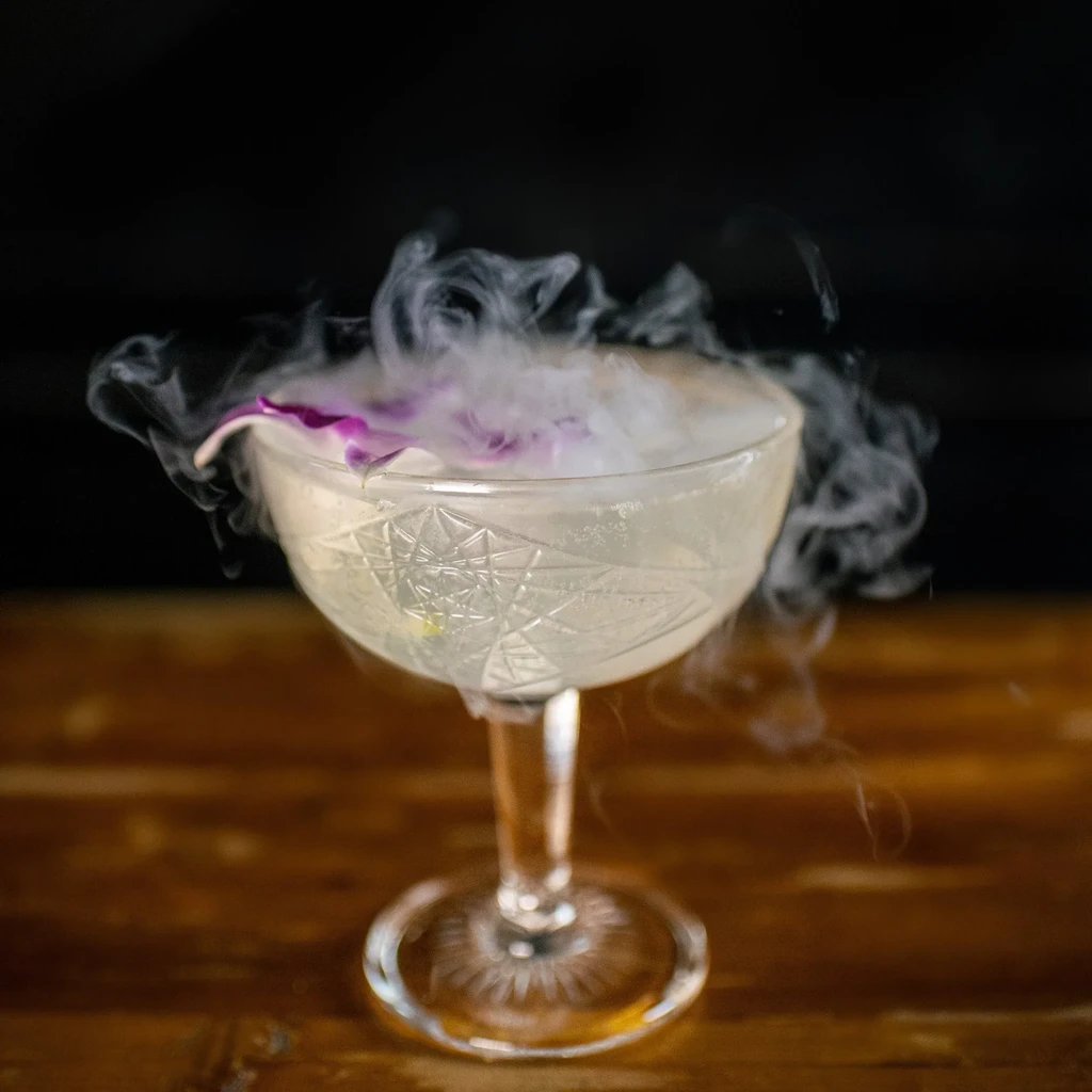 Etched coupe cocktail, purple orchid garnish, dry ice smoke.