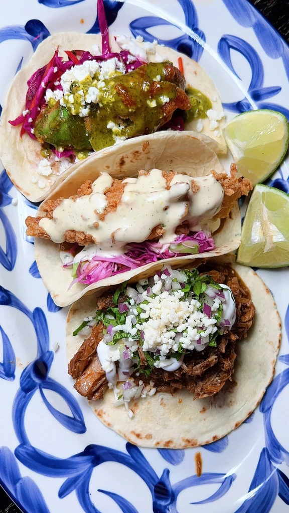 Three vibrant soft-shelled tacos with varied fillings and lime.