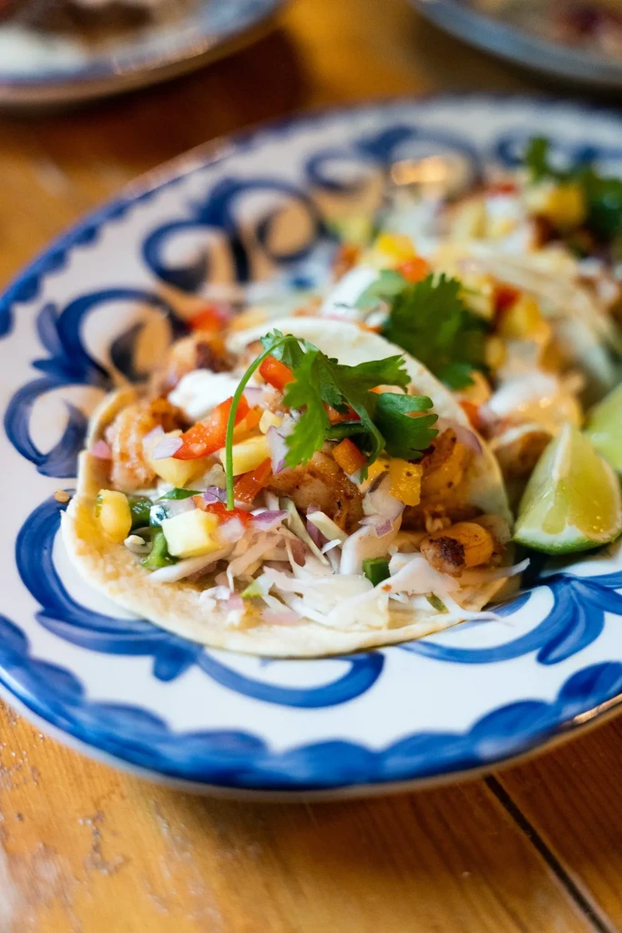 Three colorful tacos with grilled protein, vegetables, and fruit on a plate.