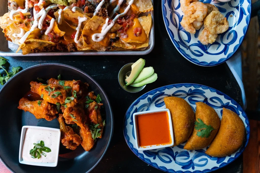 Top-down view of a varied spread of nachos, wings, empanadas, and shrimp.
