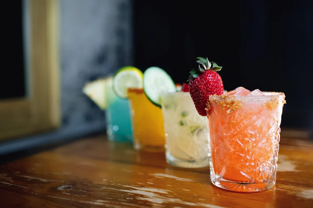 Five vibrant cocktails arranged diagonally on a dark wooden bar.