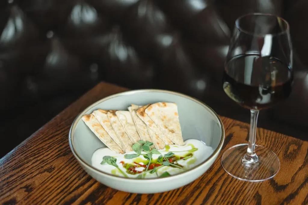 Gourmet creamy dip, flatbread, microgreens, and red wine on a table.