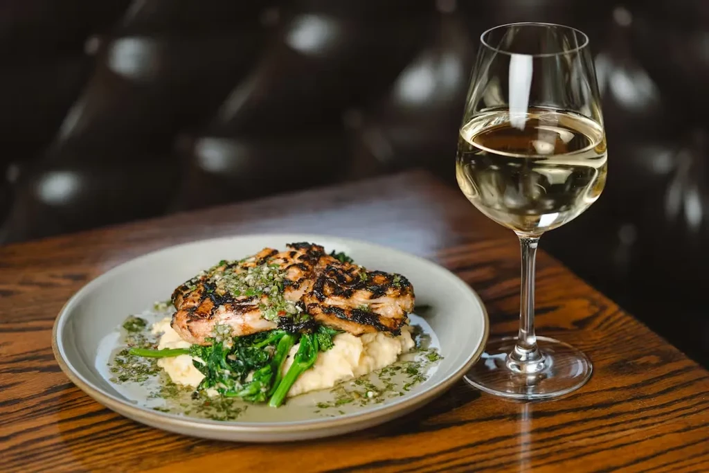 Plated grilled protein, mashed potatoes, green vegetables, and white wine.