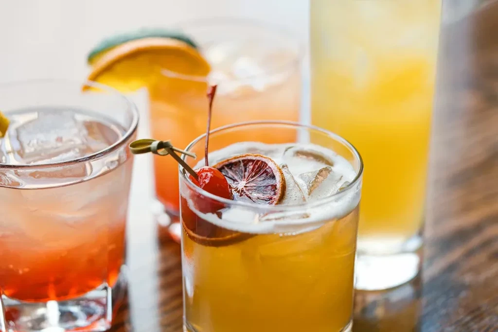 Four assorted alcoholic cocktails with ice and fruit garnishes on wood.