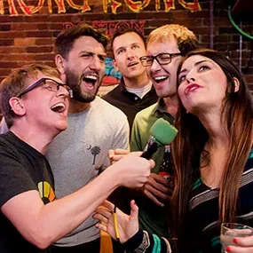 Five people enthusiastically sing into a microphone at a bar.