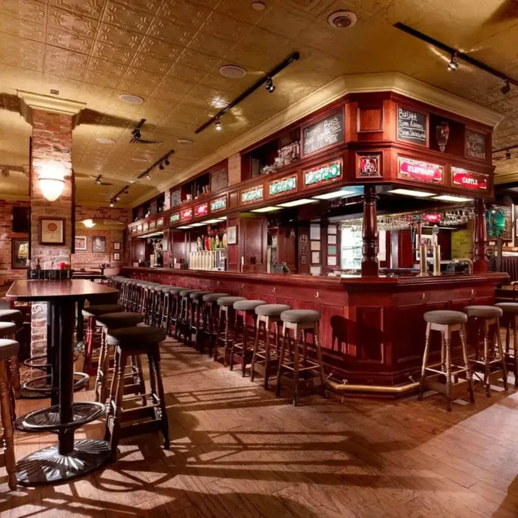 Empty, traditional pub interior with a long dark wood bar and stools.