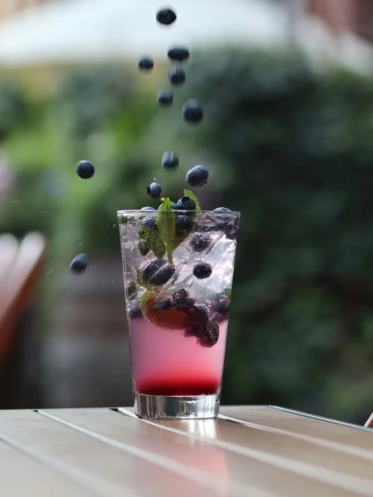 Refreshing layered drink with blueberries falling, mint, and ice.