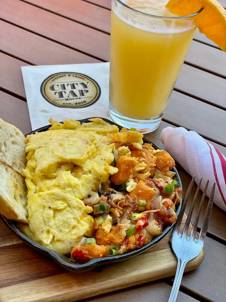 Breakfast skillet meal with eggs, sweet potato hash, toast, and orange juice.