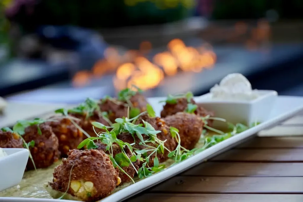 Golden-brown fritters with corn, microgreens, and white dipping sauce.