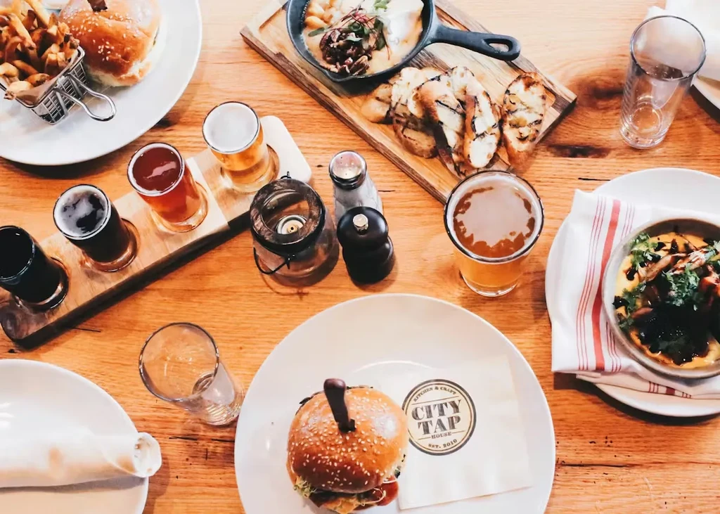 Overhead: Rustic table with burgers, fries, beer, and diverse dishes.