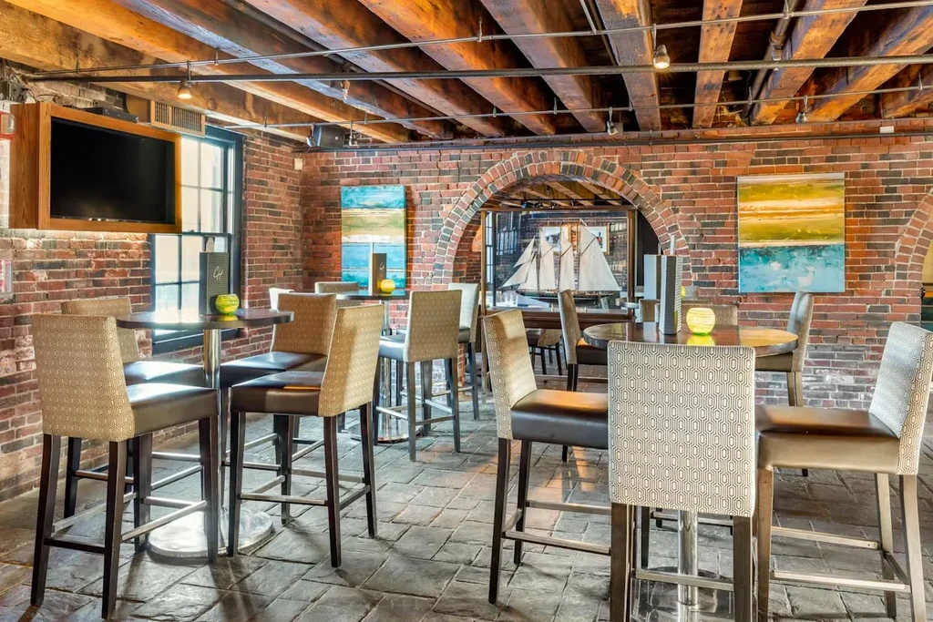 Rustic-modern bar with brick walls, wood beams, high-top tables, ship model.