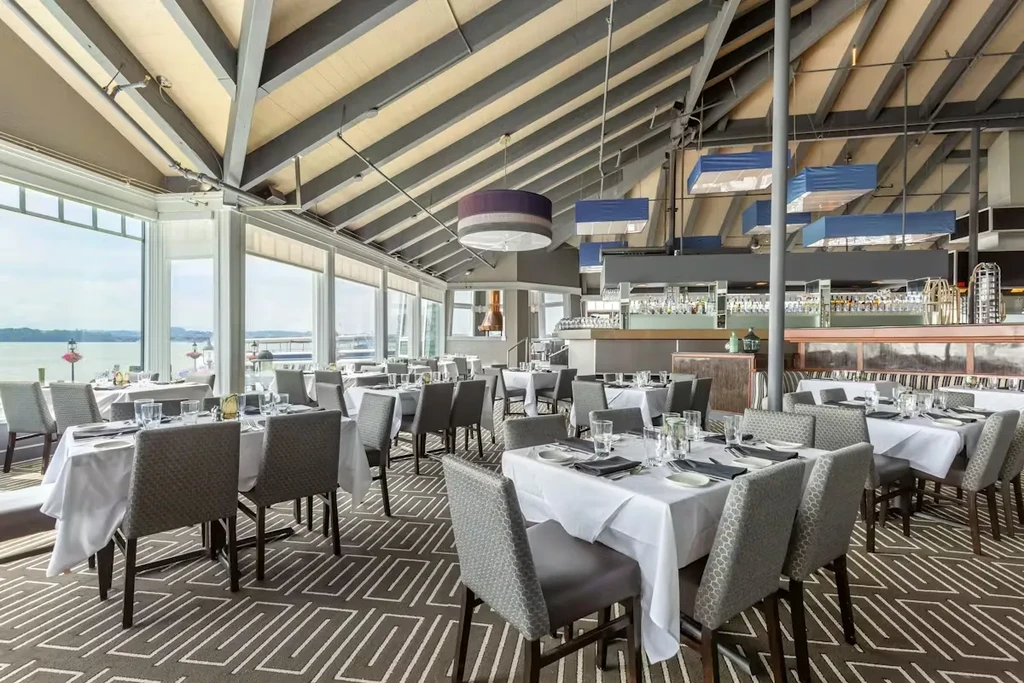Empty upscale restaurant with set tables, bar, and waterfront view.