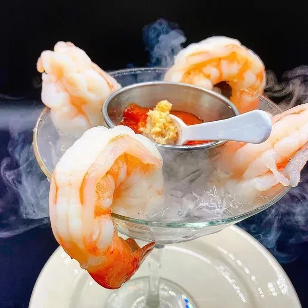 Four large shrimp cocktail in a stemmed glass with misty ice and sauces.