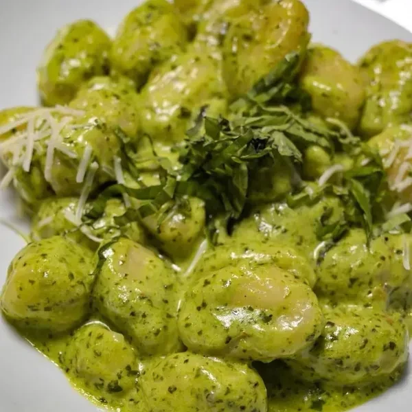 Plate of gnocchi with vibrant green pesto, fresh basil, and cheese.