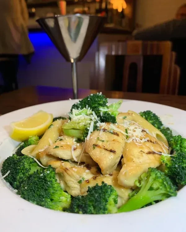 Close-up of grilled chicken pasta with broccoli, cheese, and lemon.