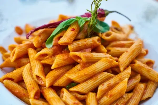 Penne pasta with reddish-orange sauce, basil, a chili, and rosemary.