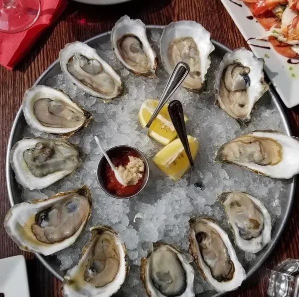 Freshly shucked oysters on ice with cocktail sauce, lemon, and forks.