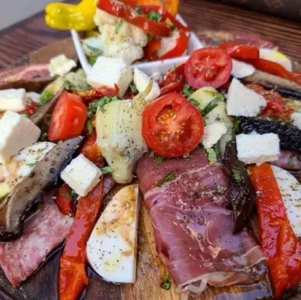 Antipasto board with meats, cheeses, tomatoes, olives, and artichokes.