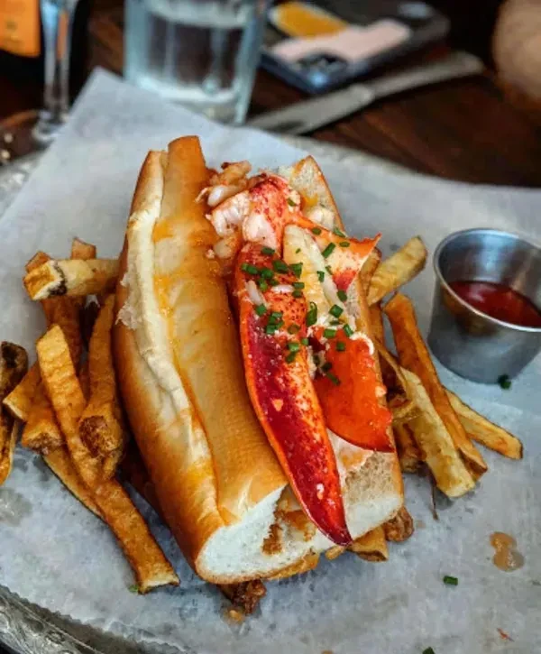 Lobster roll topped with a claw, served with french fries and ketchup.