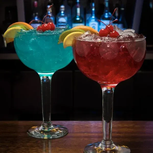 Two garnished blue and red cocktails on a wooden bar.