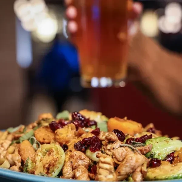 Colorful roasted meal with chicken, vegetables, cranberries on light blue plate.